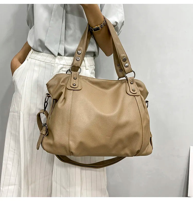 Sac à main en cuir beige porté par une femme en chemise blanche et pantalon à rayures. Mode élégante, accessoire tendance, style chic.