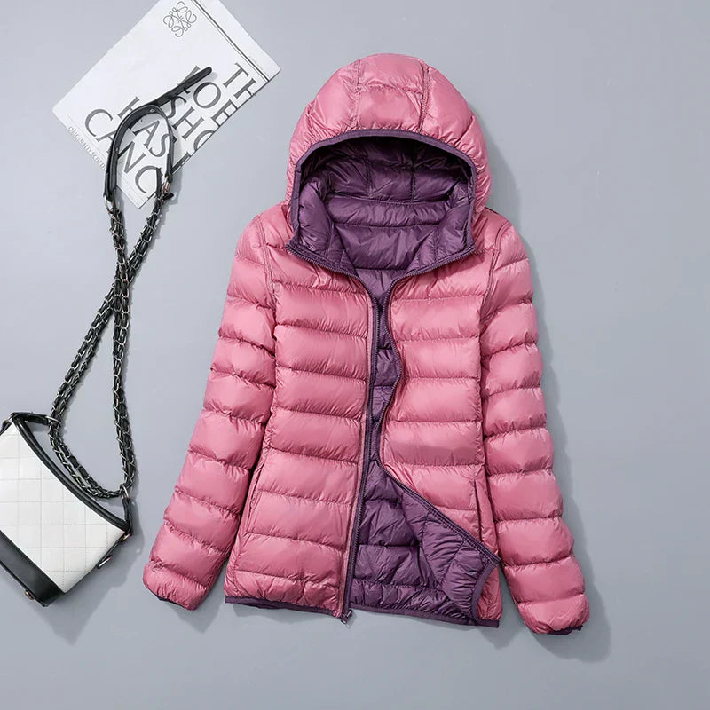 Doudoune rose à capuche avec doublure violette, posée sur fond gris, accompagnée d'un sac à main blanc et noir. Mode hiver femme élégante.