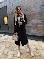 Femme élégante en manteau noir devant boutique Loewe, portant sac Prada beige et bottes assorties. Mode automne chic, style urbain sophistiqué.