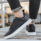 Chaussures noires en cuir synthétique avec semelles blanches, portées avec un jean noir déchiré. Style décontracté, mode urbaine, tendance sneakers.