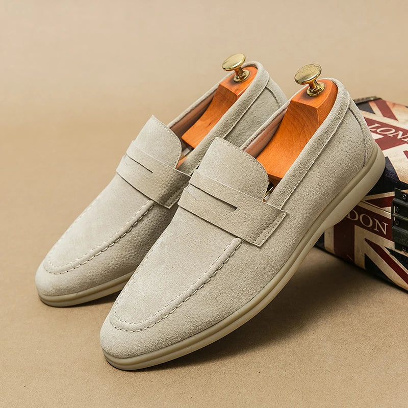 Mocassins en daim beige pour homme avec embauchoirs, posés sur une boîte décorée du drapeau britannique. Chaussures élégantes et confortables.