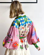 Femme portant une robe colorée avec motifs géométriques et symboles mystiques, manches bouffantes roses, fond blanc. Mode bohème chic, tendance.