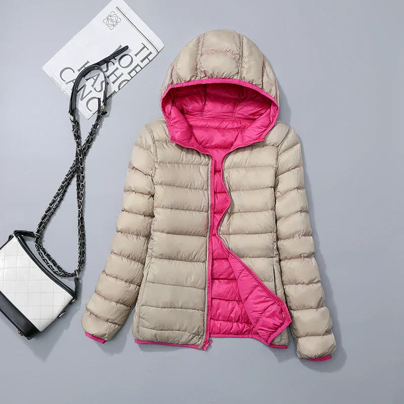 Veste matelassée beige à capuche, doublure rose vif, posée à plat avec un sac à main noir et blanc à chaîne, sur fond gris clair.