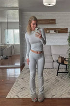 Femme en tenue de sport grise prenant un selfie dans un salon moderne avec canapé beige, tapis texturé et miroir.
