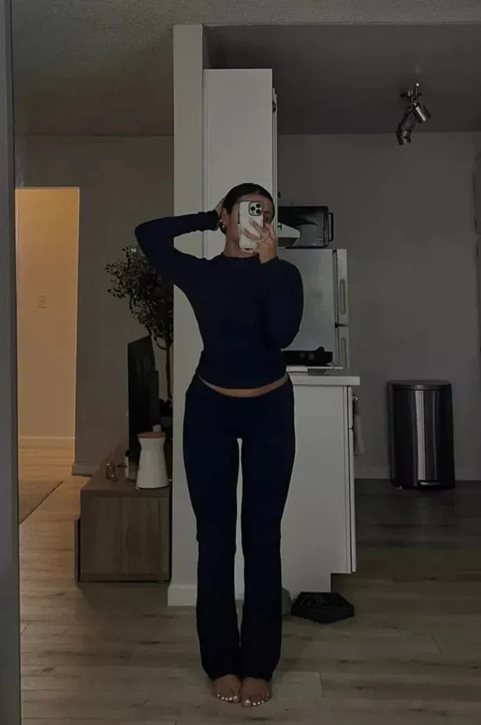 Femme en tenue de sport noire prenant un selfie dans un miroir, intérieur moderne, éclairage tamisé, décoration minimaliste, ambiance décontractée.