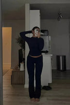 Femme en tenue de sport noire prenant un selfie dans un miroir, intérieur moderne, éclairage tamisé, décoration minimaliste, ambiance décontractée.