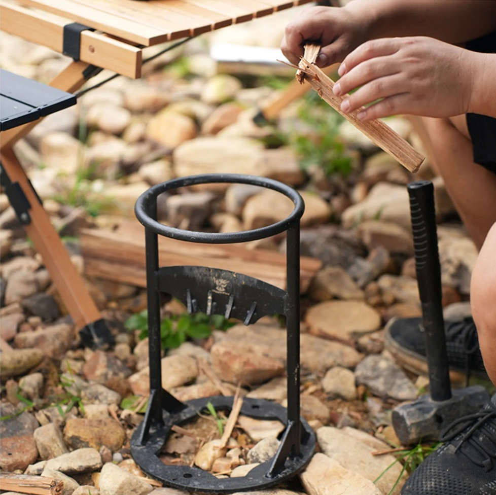 Personne utilisant un coupe-bûches manuel sur des pierres, avec une table pliante en bois à côté. Outil de camping, préparation de bois de chauffage.