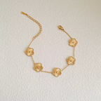 Bracelet en or avec cinq pendentifs en forme de fleur, chaîne délicate et fermoir mousqueton, posé sur une surface texturée. Accessoire élégant.