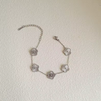 Bracelet en argent avec cinq pendentifs en forme de fleur, chaîne ajustable, posé sur une surface blanche texturée. Accessoire élégant et tendance.