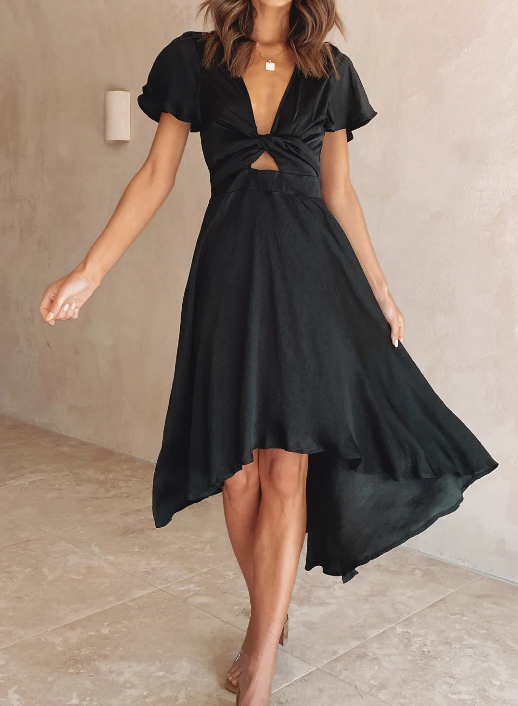 Robe noire élégante avec découpe frontale, manches courtes et ourlet asymétrique, portée par une femme sur fond neutre. Mode féminine chic.