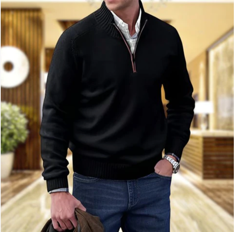 Homme portant un pull noir élégant avec col zippé, chemise blanche, jeans bleu, tenant une veste marron. Mode masculine décontractée et chic.