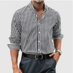 Chemise à rayures noires et blanches pour homme, manches longues retroussées, portée avec un pantalon gris et une ceinture noire. Style élégant et moderne.