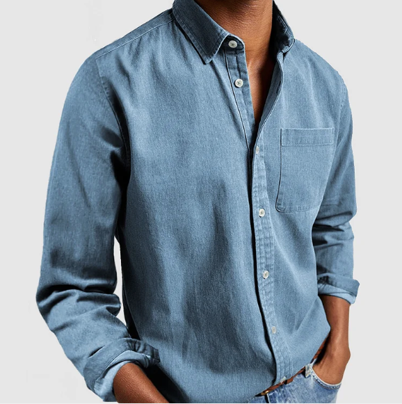 Chemise en jean bleu pour homme, manches longues, poche poitrine, style décontracté, mode masculine, tenue élégante, fond gris clair.
