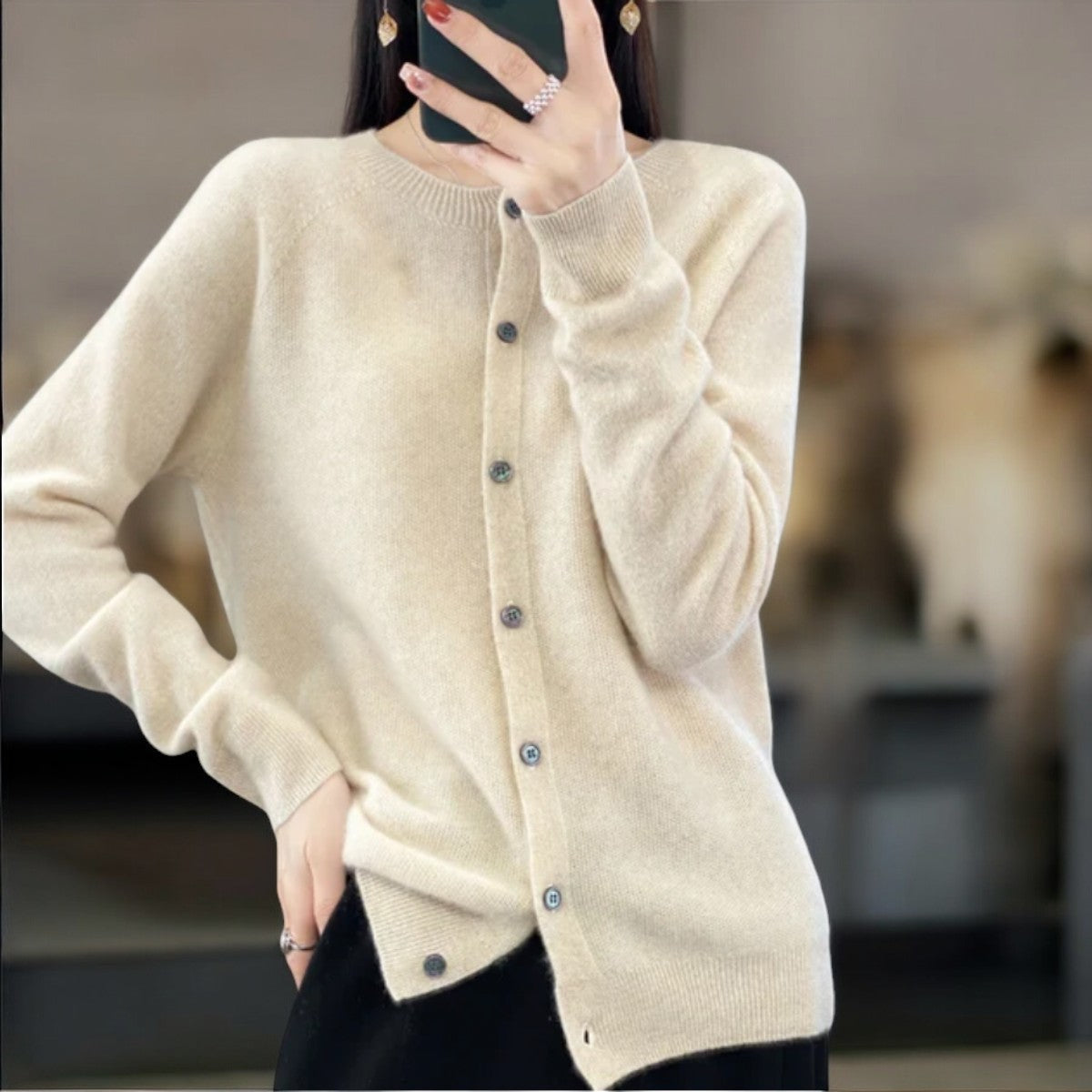 Femme portant un cardigan beige en cachemire, boutonné, manches longues, avec fond flou. Mode automne-hiver, élégance, confort.