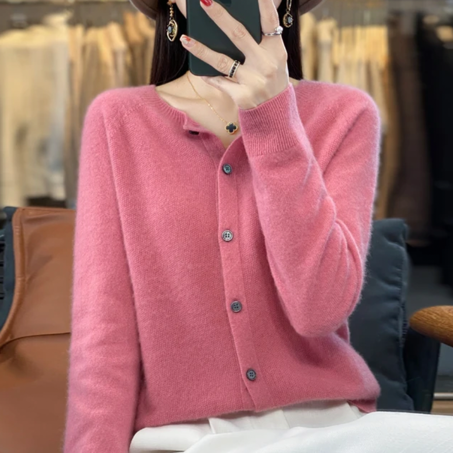 Femme portant un cardigan rose en cachemire, assise dans un magasin de vêtements. Mode automne-hiver, élégance féminine, style décontracté.