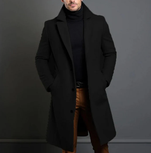 Homme portant un manteau noir élégant, col relevé, sur un pull noir et un pantalon beige. Mode masculine chic, style automne-hiver.