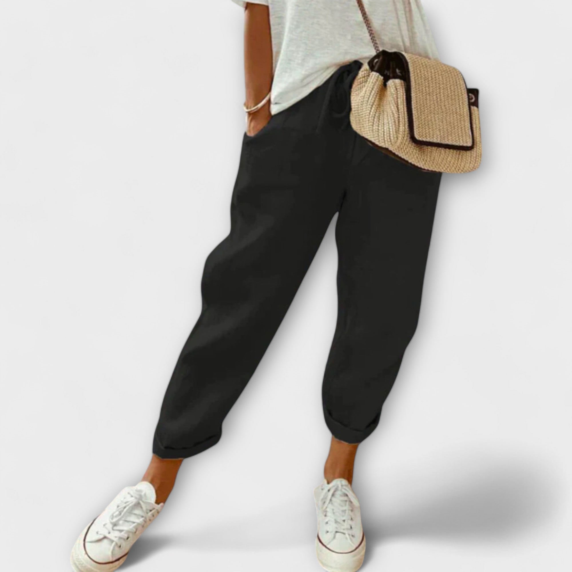 Femme portant un pantalon noir ample, t-shirt blanc, baskets blanches et sac en osier. Mode décontractée, style estival, tenue confortable.