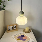 Lampe suspendue moderne éclairée, design minimaliste, à côté d'un calendrier en bois affichant le 30 août, sur une table avec une bougie cube.