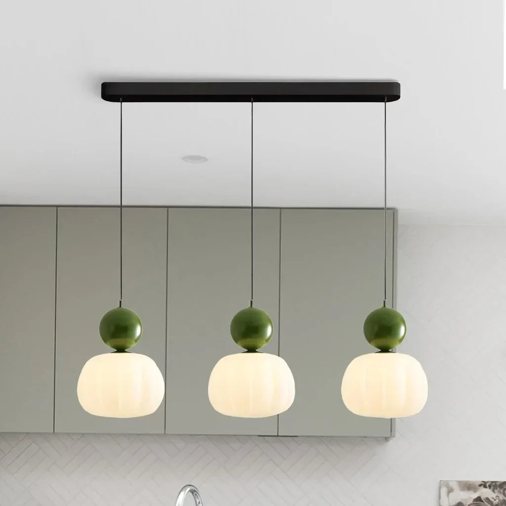 Suspension moderne à trois lumières avec abat-jours blancs et détails verts, idéale pour cuisine contemporaine. Éclairage design intérieur.