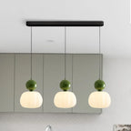 Suspension moderne à trois lumières avec abat-jours blancs et détails verts, idéale pour cuisine contemporaine. Éclairage design intérieur.