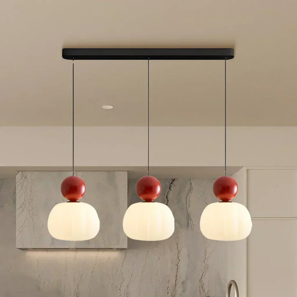 Suspension moderne à trois lumières avec abat-jours blancs et détails rouges, idéale pour cuisine contemporaine, éclairage intérieur design.