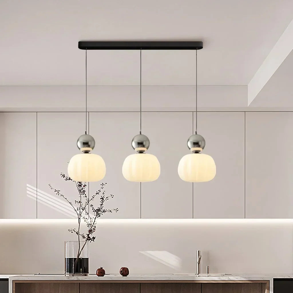 Suspension moderne à trois lampes avec abat-jours en verre opale, installée dans une cuisine contemporaine, éclairage design et élégant.