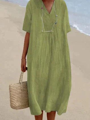 Robe verte ample en lin portée par une femme sur la plage, tenant un sac en osier. Mode estivale, tenue décontractée, style plage chic.