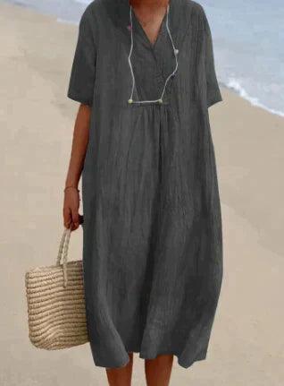 Robe d'été grise ample sur plage, femme tenant un sac en osier. Mode plage, tenue décontractée, style estival chic.