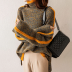 Femme portant un pull en maille rayé gris et orange, avec un sac à main noir matelassé. Mode automne, style décontracté chic.