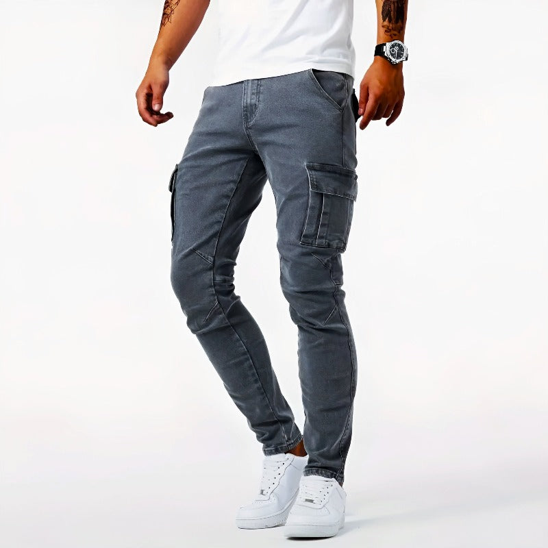 Pantalon cargo gris pour homme, coupe ajustée, poches latérales, porté avec des baskets blanches et un t-shirt blanc. Mode masculine décontractée.