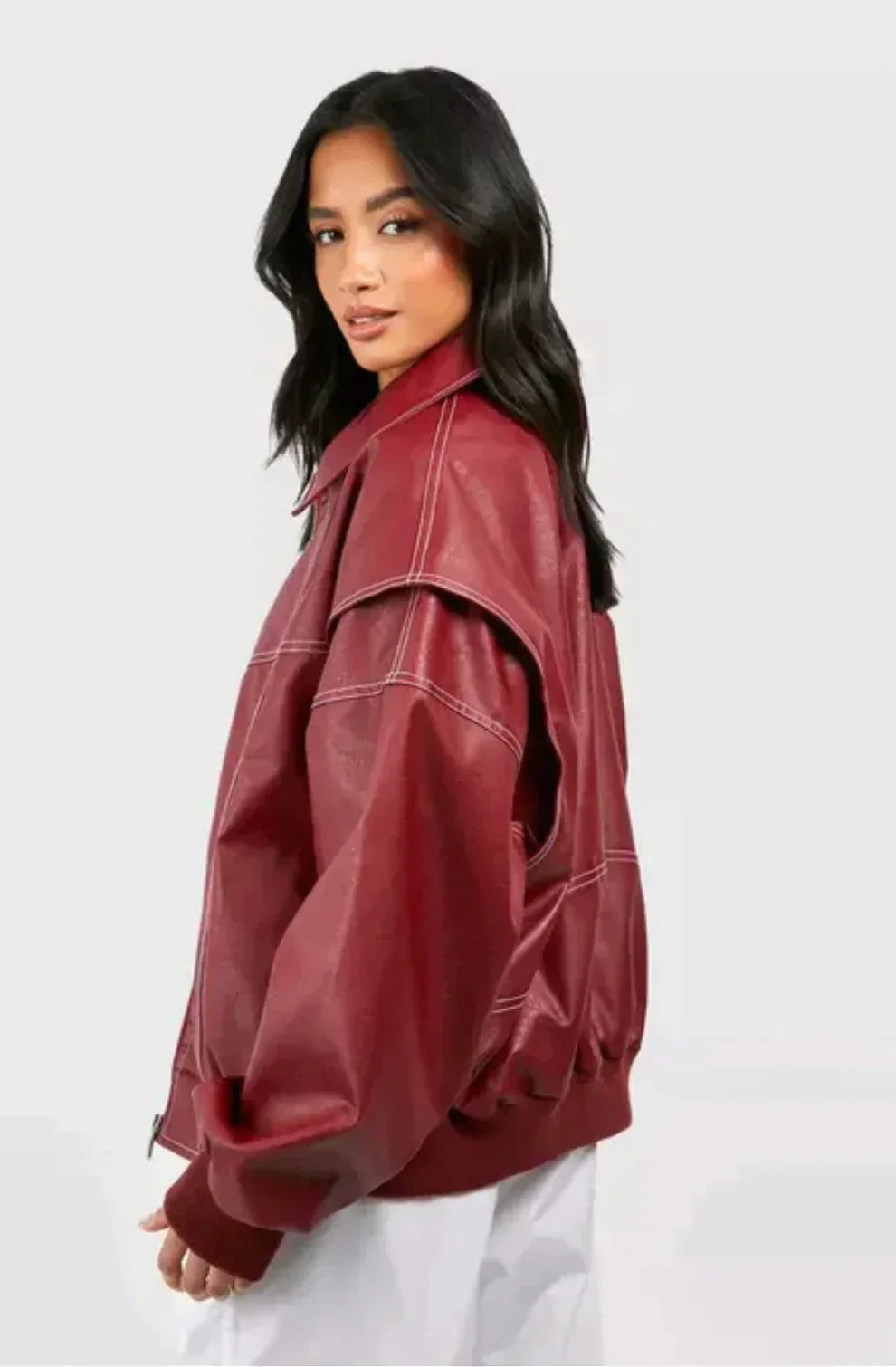 Femme portant une veste en cuir rouge bordeaux, coupe ample, avec coutures apparentes, sur fond blanc. Mode automne, tendance vestimentaire.