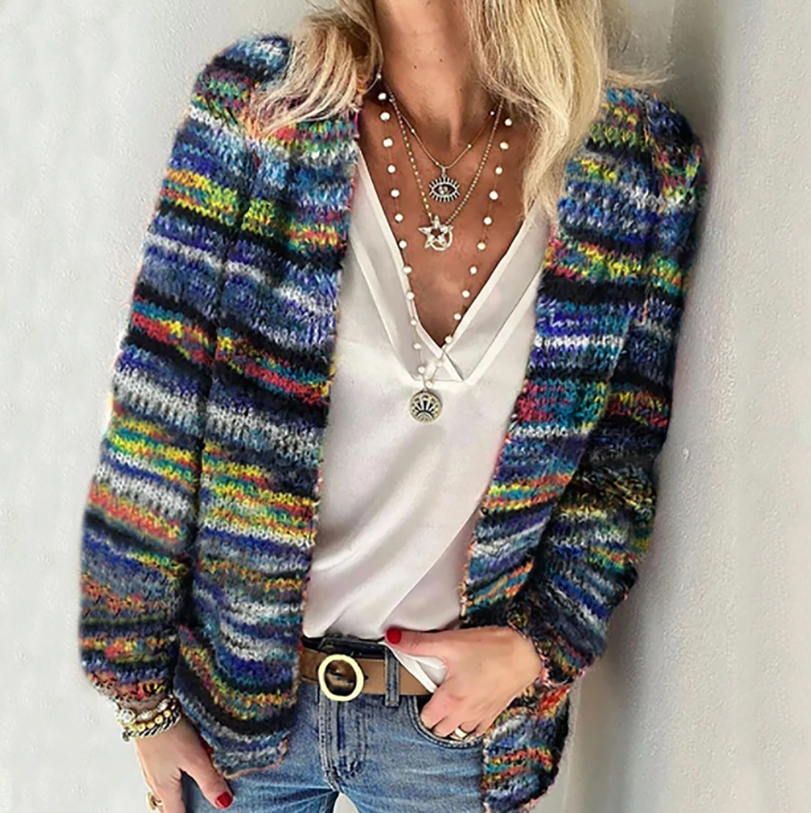 Femme portant un cardigan multicolore en laine, t-shirt blanc, colliers superposés, et jeans. Mode automne, style décontracté, tendance 2023.
