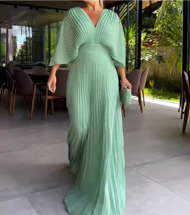 Robe longue plissée vert menthe élégante, manches évasées, portée par une femme dans un intérieur moderne. Mode féminine chic et tendance.