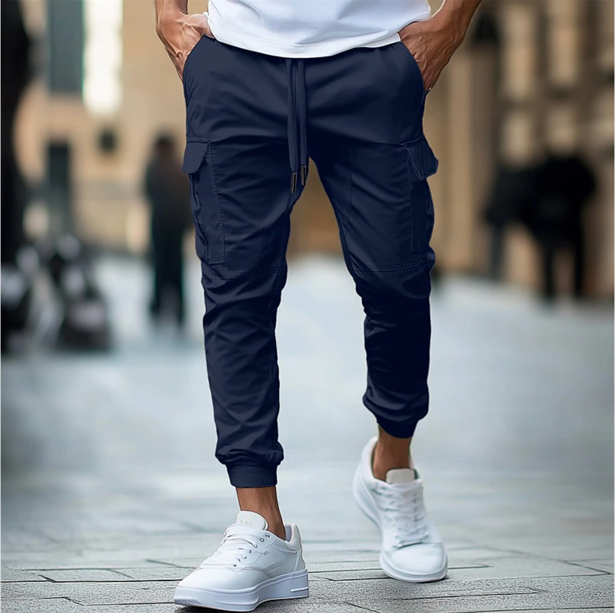 Homme portant un pantalon cargo bleu marine et des baskets blanches, marchant en ville. Mode urbaine, style décontracté, tendance masculine.