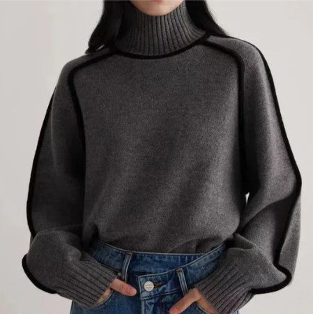 Femme portant un pull gris à col roulé avec bordures noires, manches longues, associé à un jean bleu. Mode automne-hiver, style décontracté.