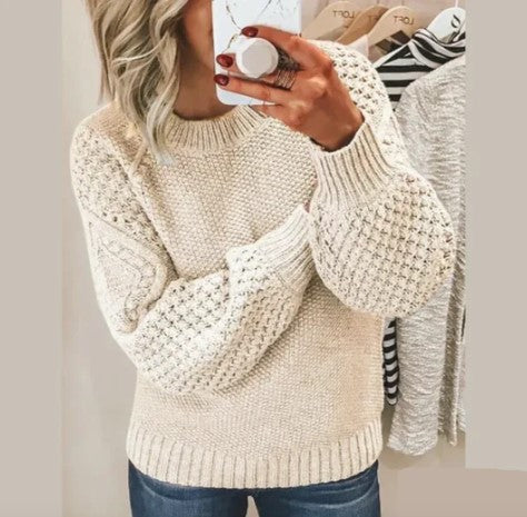 Femme portant un pull en tricot beige texturé, manches longues, tenant un smartphone, mode automne-hiver, style décontracté, tendance féminine.