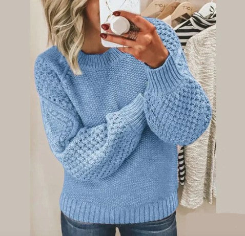 Femme portant un pull bleu en tricot torsadé, manches longues, devant un miroir. Mode automne-hiver, style décontracté, tendance féminine.