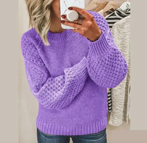 Femme portant un pull violet en tricot texturé, manches longues, tenant un smartphone. Mode automne-hiver, style décontracté, tendance féminine.