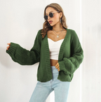 Femme portant un cardigan vert ample, lunettes de soleil, top blanc et jean clair. Mode automne, style décontracté, tendance féminine.