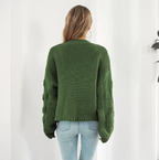 Femme portant un pull vert en tricot avec manches texturées, vue de dos, jeans bleu clair, style décontracté, mode automne-hiver.