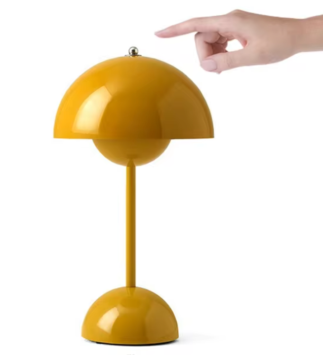 Lampe de table design rétro jaune moutarde avec abat-jour hémisphérique, interrupteur à bouton, main ajustant l'éclairage. Décoration intérieure moderne.