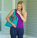 Femme souriante portant un chat gris dans un sac en tissu turquoise, debout devant une maison. Accessoire pratique pour animaux de compagnie.