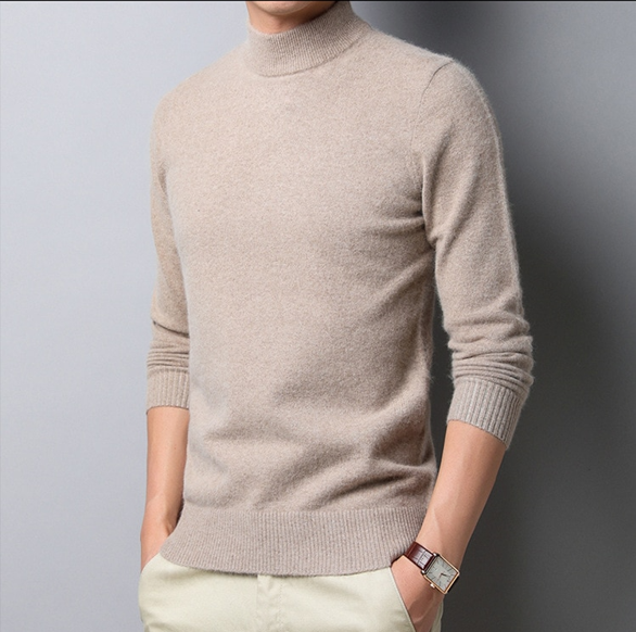 Homme portant un pull col roulé beige en cachemire, manches longues, avec montre-bracelet marron, sur fond gris. Mode masculine élégante.