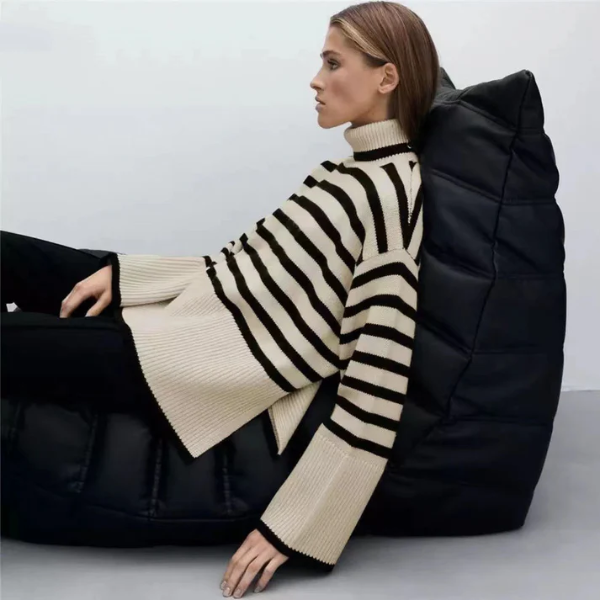 Femme assise sur un pouf noir, portant un pull à rayures noires et blanches, style moderne et décontracté, mode automne-hiver.