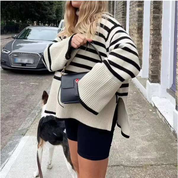Femme en pull rayé noir et blanc, tenant un sac à main noir, avec un chien en laisse, devant une voiture garée sur un trottoir urbain.