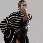 Femme portant un pull rayé noir et blanc, lunettes de soleil, prenant un selfie avec un smartphone, style moderne et chic, mode automne-hiver.