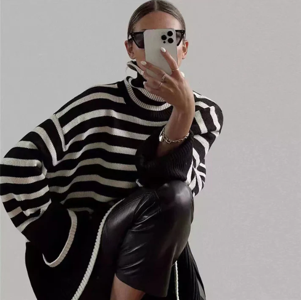 Femme portant un pull rayé noir et blanc, lunettes de soleil, prenant un selfie avec un smartphone, style moderne et chic, mode automne-hiver.