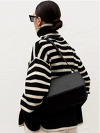 Femme portant un pull rayé noir et blanc, lunettes de soleil noires, sac à main noir, cheveux attachés en chignon, style mode automne-hiver.
