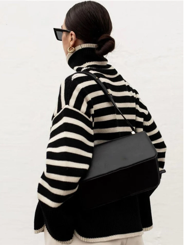 Femme portant un pull rayé noir et blanc, lunettes de soleil noires, sac à main noir, cheveux attachés en chignon, style mode automne-hiver.