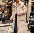 Femme portant un long manteau d'hiver beige, tenant un sac à main blanc, marchant en ville. Mode urbaine, tendance hiver, style élégant.